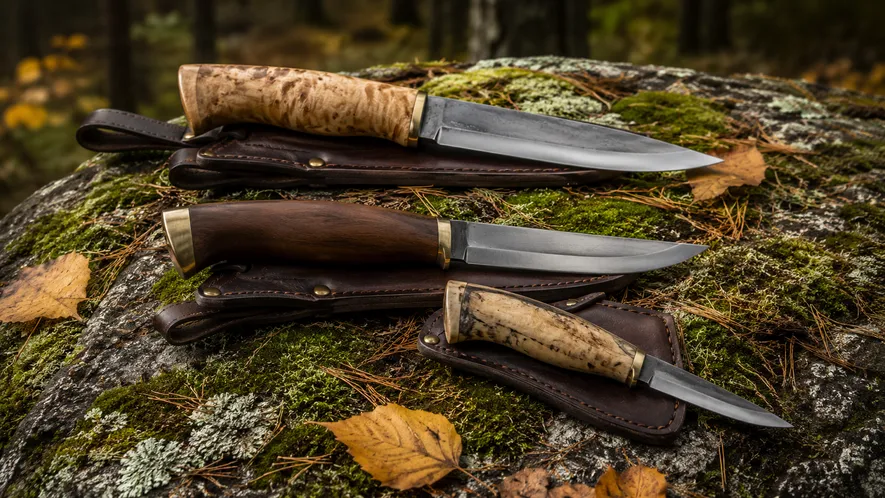 Svenske friluftskniver med trehåndtak lagt på mosegrodd stein i skogen